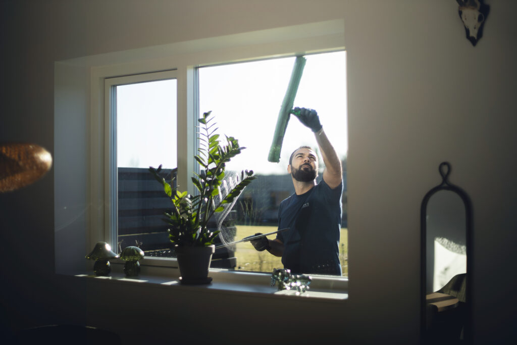 Mand pudser vinduer med planter i vindueskarmen